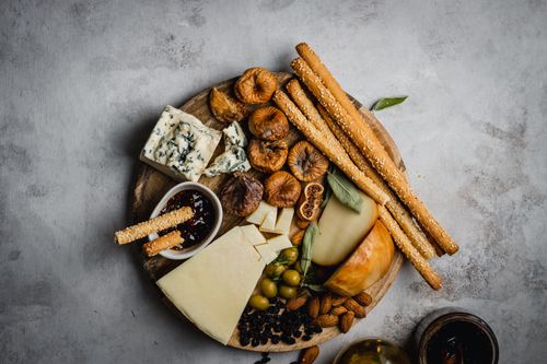 Free A top view of a rustic charcuterie board featuring cheese, dried figs, breadsticks, and olives. Stock Photo