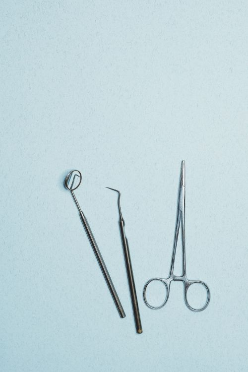 Free Stainless steel dental instruments arranged on a blue surface, featuring a mirror, excavator, and plier. Stock Photo