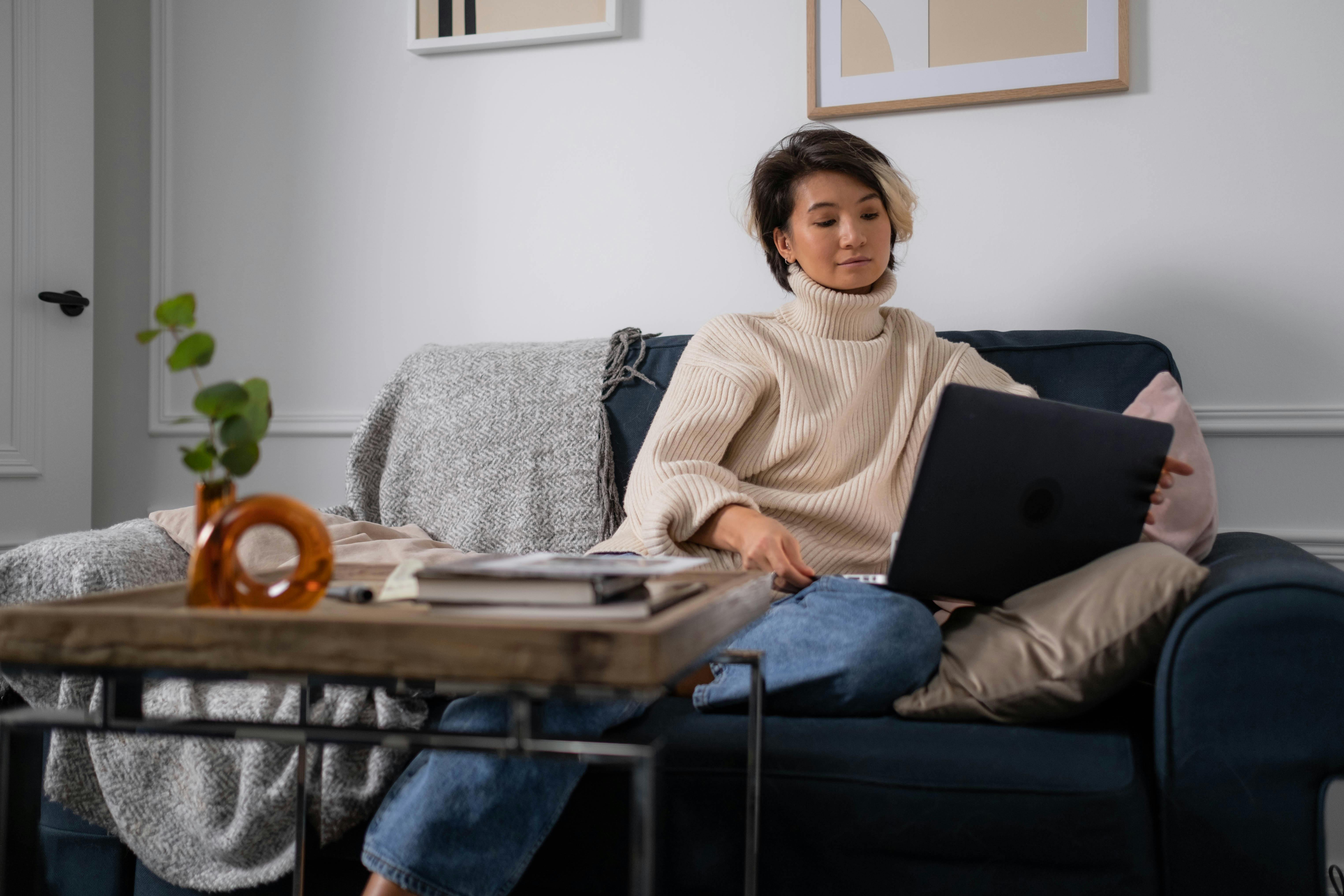 a woman in a sweater using a laptop while sitting on a couch