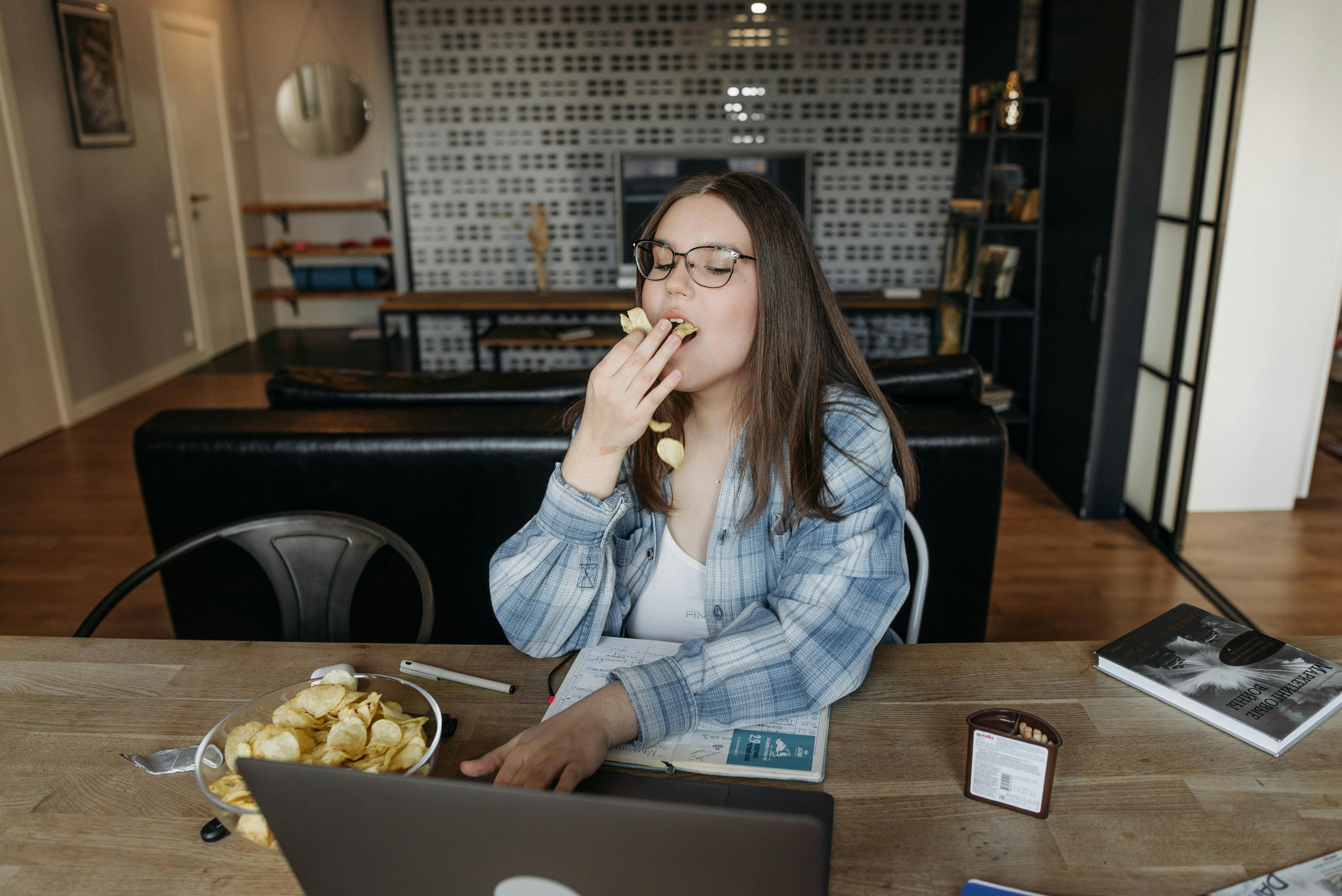 A Woman Eating Chips While Using Her Laptop · Free Stock Photo