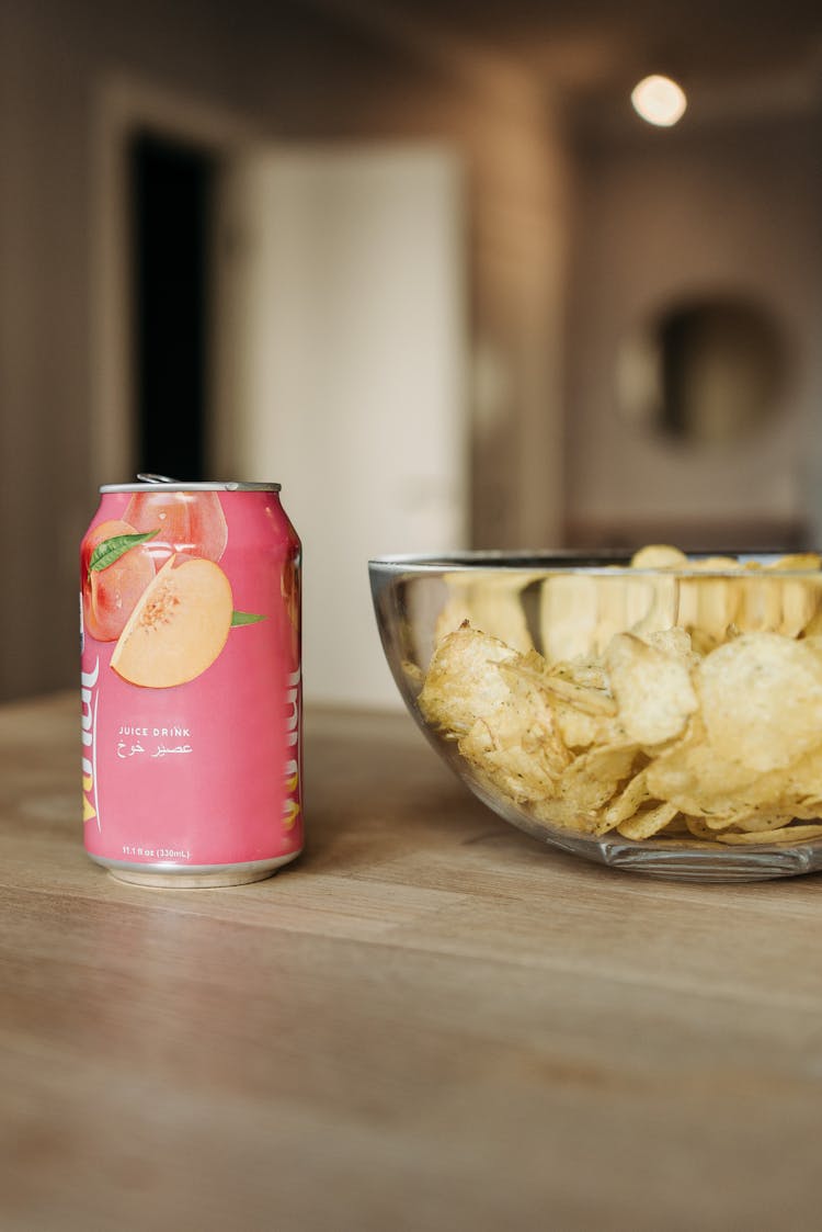 A Close-Up Shot Of A Canned Drink And A Bowl Of Chips