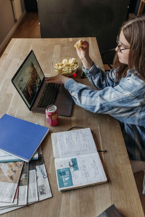 Free Woman working from home with a laptop, notebooks, and snacks on a table. Stock Photo
