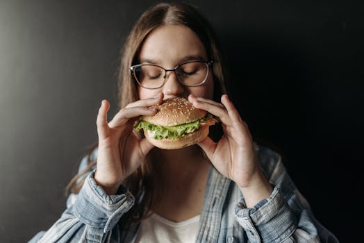 Young woman savoring a fresh burger indoors, depicting enjoyment of fast food.