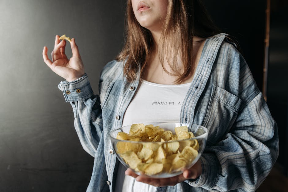Woman in plaid shirt holding a bowl of potato chips indoors. Casual lifestyle image.