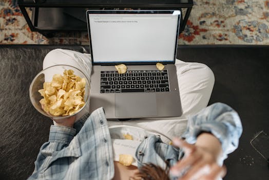 An adult woman enjoying chips while using a laptop indoors, creating a cozy setting.