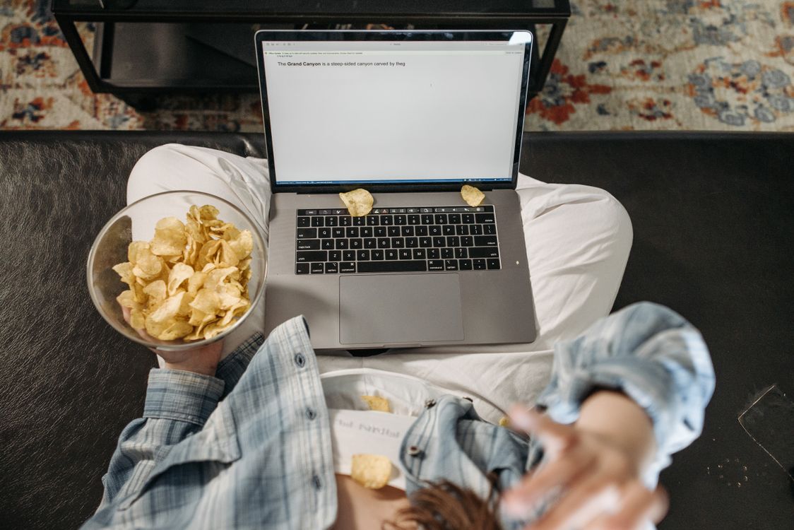 A Woman Eating Chips while Using a Laptop · Free Stock Photo