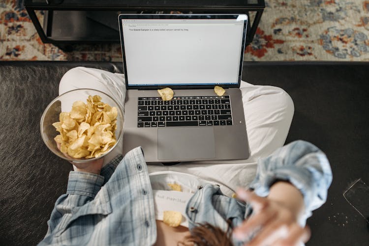 A Woman Eating Chips While Using A Laptop