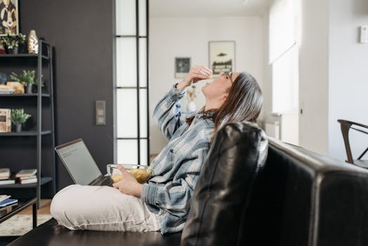 Woman enjoying snacks while working from home on laptop.
