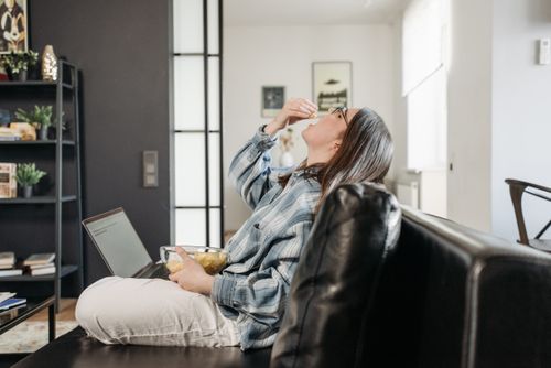 Free Woman enjoying snacks while working from home on laptop. Stock Photo