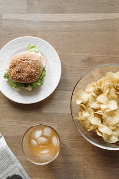 A bird's-eye view of a burger, chips, and a drink on a wooden table for a casual meal setup.