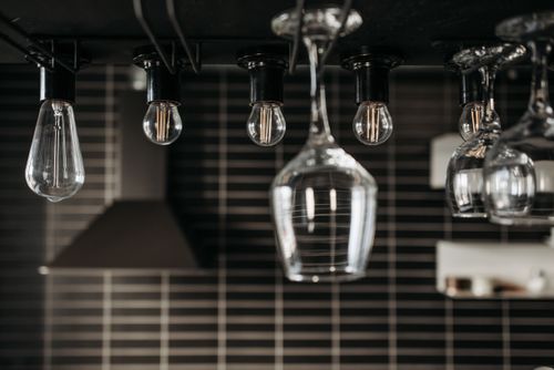 Free Stylish arrangement of hanging light bulbs and wine glasses in a modern interior setting. Stock Photo