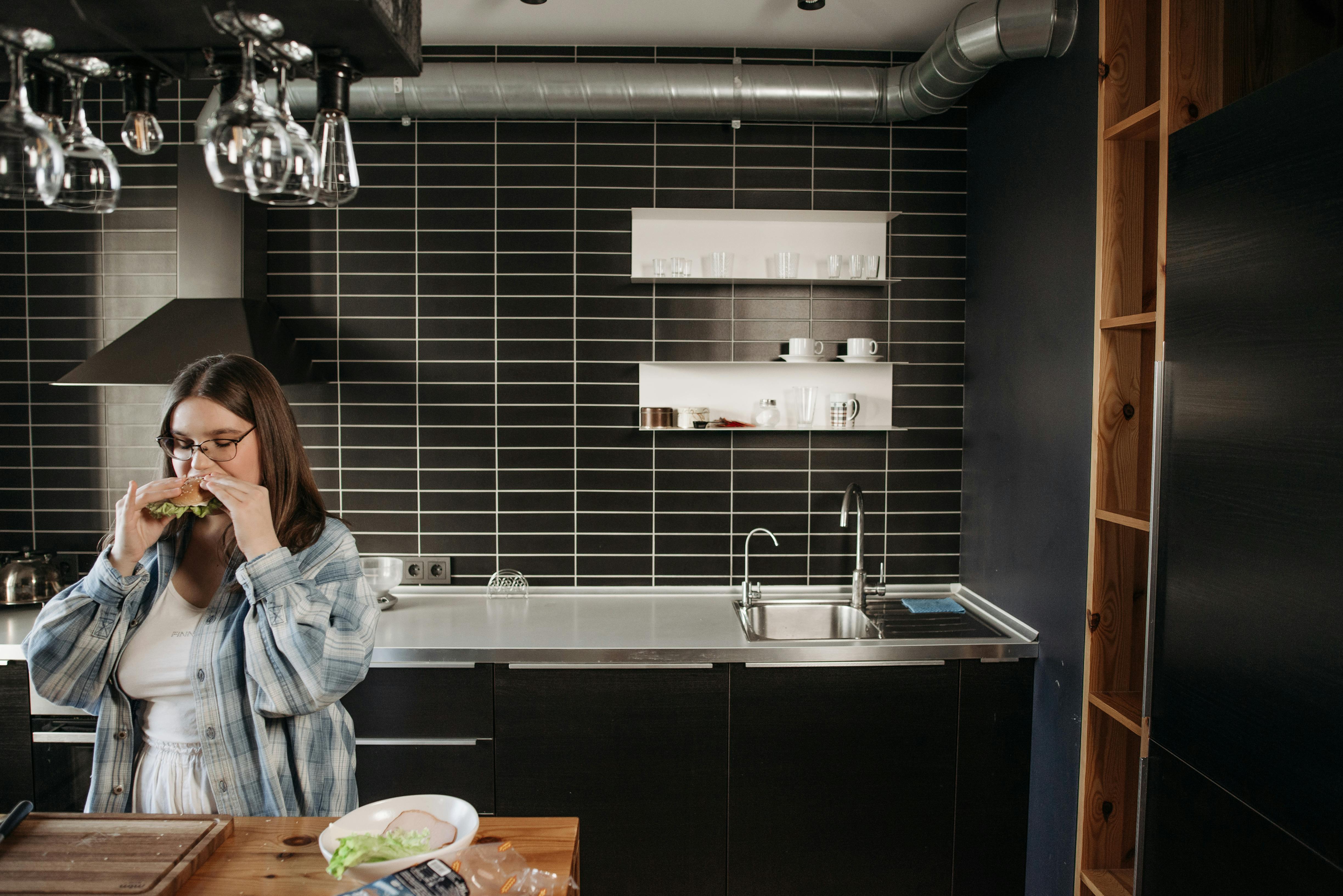 Woman enjoying a sandwich in a stylish modern kitchen, showcasing contemporary design.