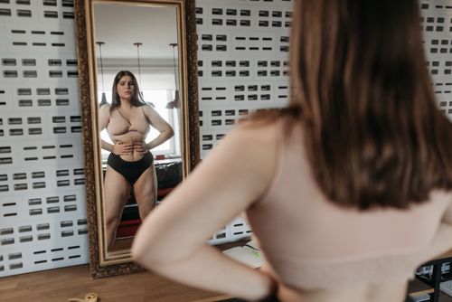 Free Woman in underwear looking at her reflection in a mirror, contemplating body image. Stock Photo