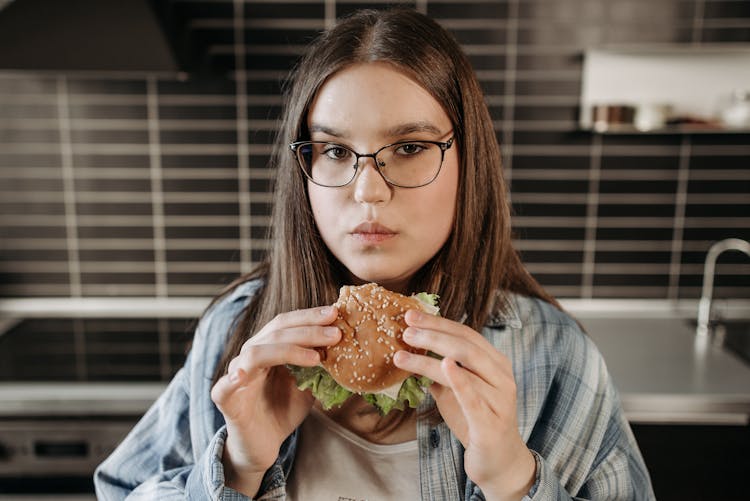 Woman In Blue And White Long Sleeve Shirt Eating A Burger