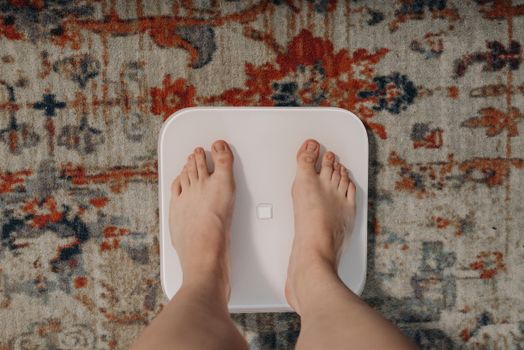 Overhead view of feet on a smart scale atop a decorative carpet, focusing on balance and health.