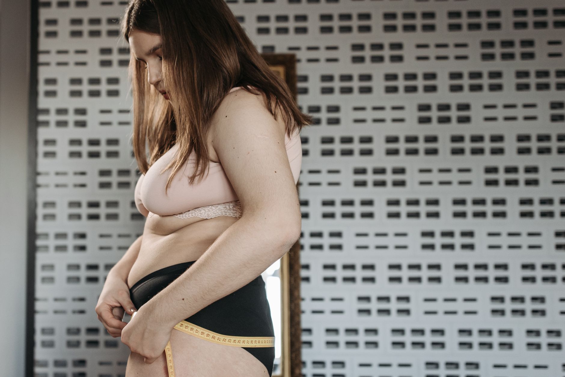Jeune femme confiante mesure ses hanches dans un intérieur élégant, célébrant la positivité corporelle.