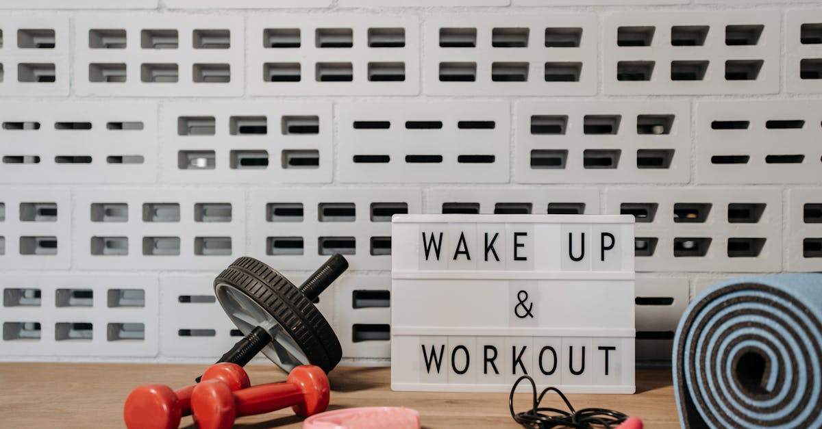 Fitness equipment display with dumbbells, an ab roller, a pink foam roller, and a yoga mat, featuring a sign that reads "WAKE UP & WORKOUT," emphasizing home gym motivation and wellness.