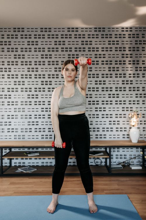 Free A woman in activewear lifting dumbbells indoors for a healthy lifestyle. Stock Photo