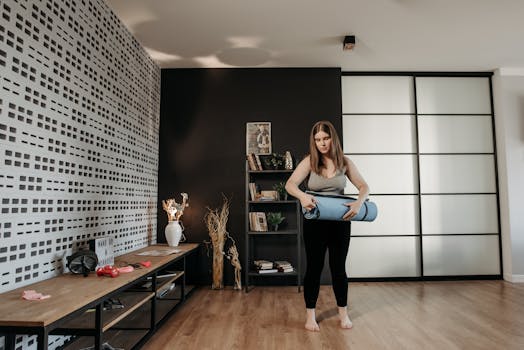 Plus size woman rolling a yoga mat in a stylish indoor setting with modern decor.