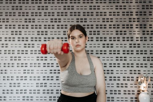 Free Focused woman in activewear lifting a dumbbell indoors, showcasing strength and determination. Stock Photo