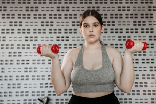 Free Confident woman exercising indoors with red dumbbells, focusing on strength training and fitness. Stock Photo