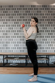 Young woman exercising with a red dumbbell inside a modern gym setting, side view.