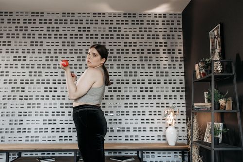 Free Adult woman exercising with a dumbbell indoors, standing in front of a patterned wall. Stock Photo