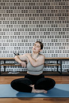 Woman seated on a yoga mat performing stretching exercises indoors.