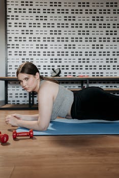 A woman doing plank exercises indoors with dumbbells on a yoga mat.