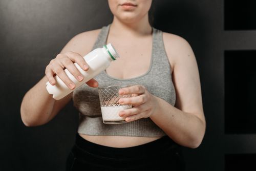 Free Close-up of woman in grey top pouring milk into glass, reflecting healthy lifestyle. Stock Photo