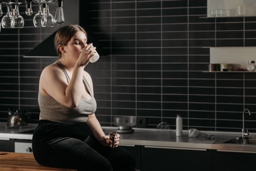Free Woman sitting on kitchen counter drinking milk in a modern setting. Stock Photo