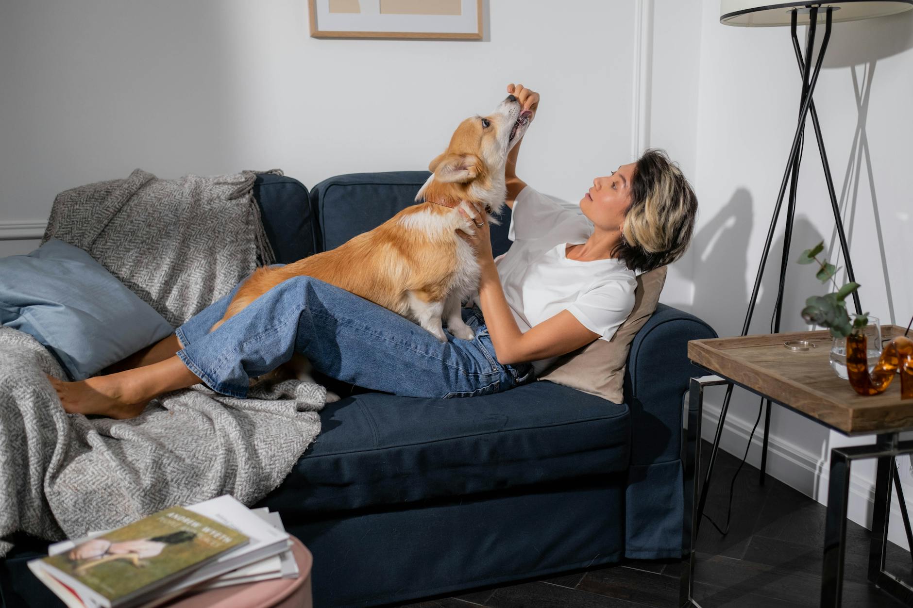 An adult woman relaxing on a sofa with her corgi dog at home, enjoying a quiet moment together.