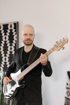 A man in a suit playing a black bass guitar indoors, showcasing musical talent.