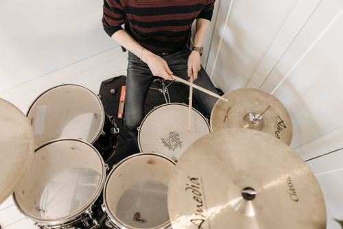 Free Overhead view of a percussionist playing drums with drumsticks, wearing a striped shirt and denim pants. Stock Photo
