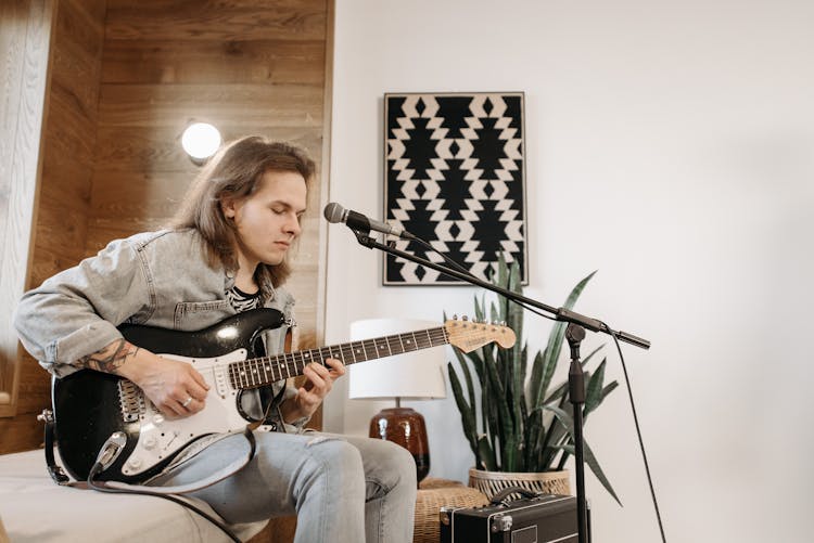 A Man Playing The Guitar While Sitting Indoors