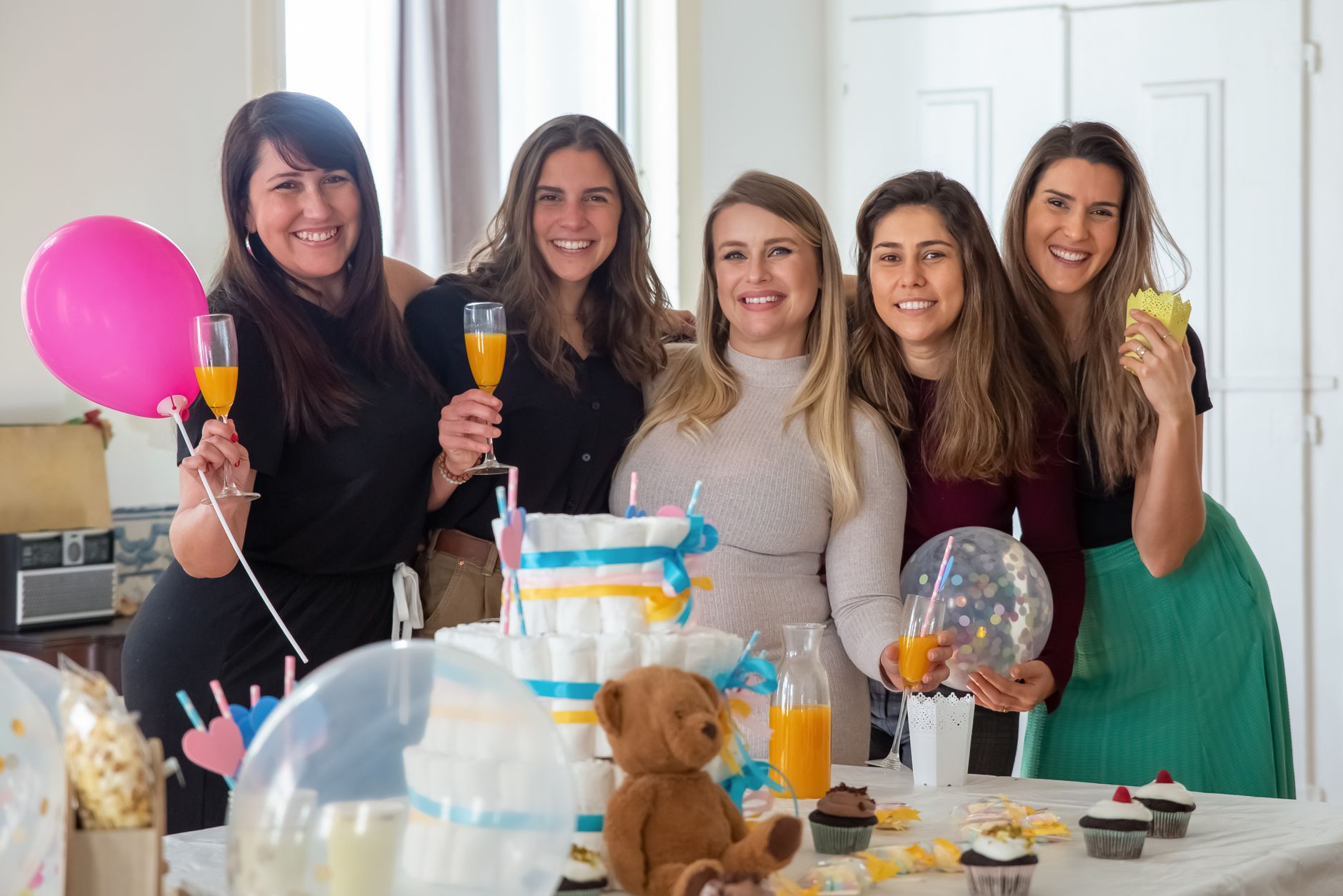 Group of women celebrating a cheerful baby shower indoors with decorations and refreshments.