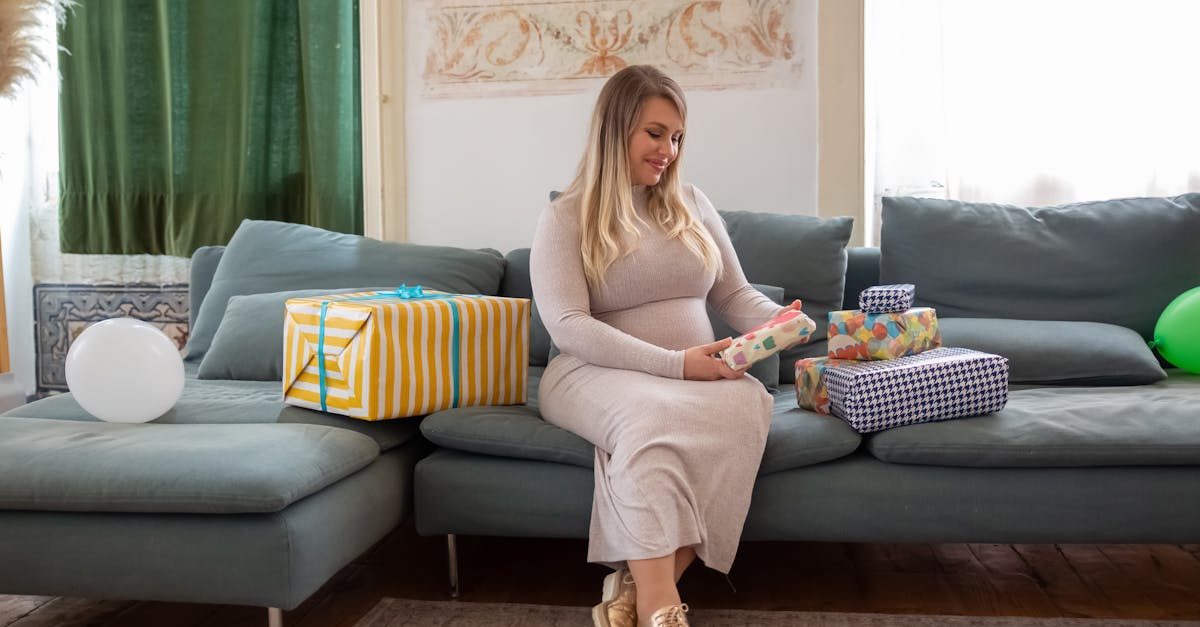 A pregnant woman joyfully opens gifts during a baby shower at home.