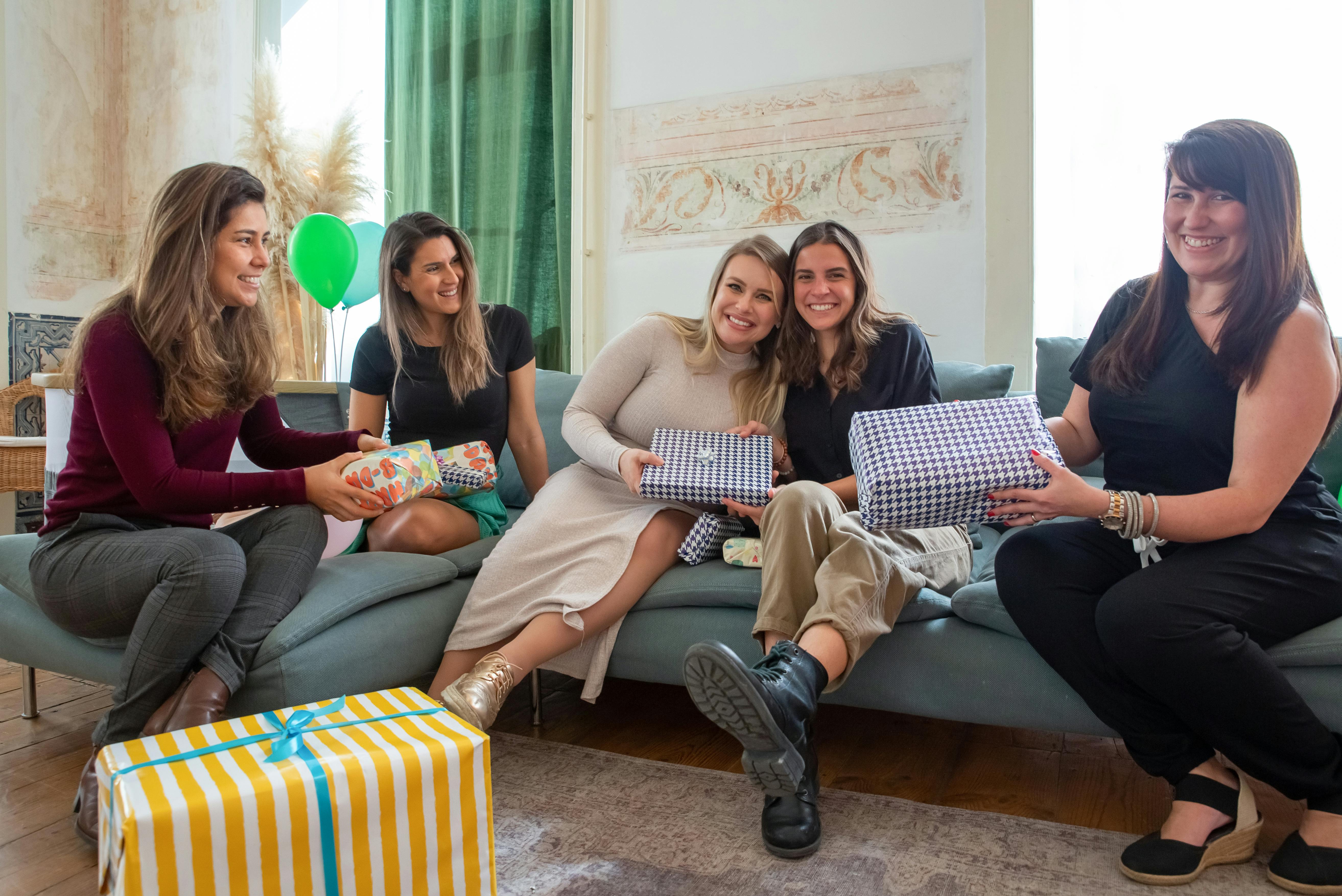 Five women enjoying a cheerful gift exchange at a cozy indoor gathering.