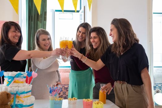 Group of women celebrating a baby shower with orange juice toasts and decorations.