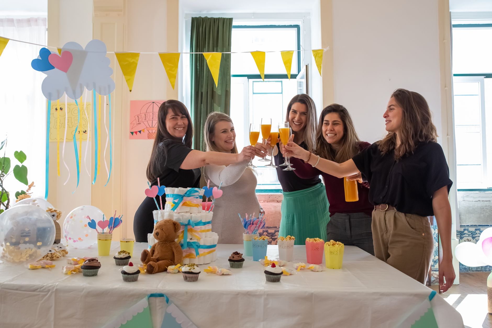 Group of women celebrating a baby shower with drinks and decorations indoors.