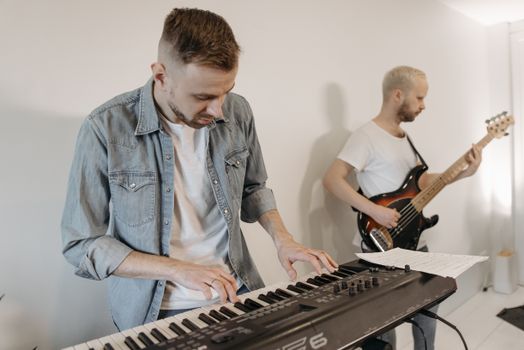 Two musicians rehearsing indoors, playing keyboard and bass guitar in a casual setting.