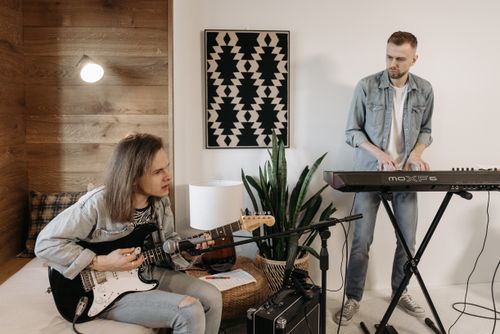 Free Two musicians playing guitar and keyboard in cozy home setting. Perfect for a relaxed vibe. Stock Photo