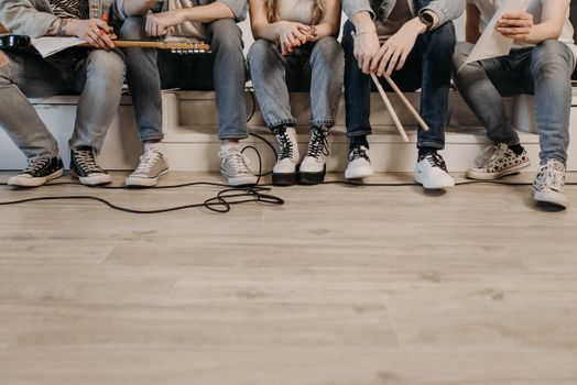 Group of musicians sitting in a casual setting ready for band rehearsal, wearing denim and sneakers.