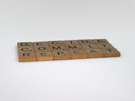 Wooden tiles arranged to spell 'DECIDE COMMIT REPEAT' on a white background.