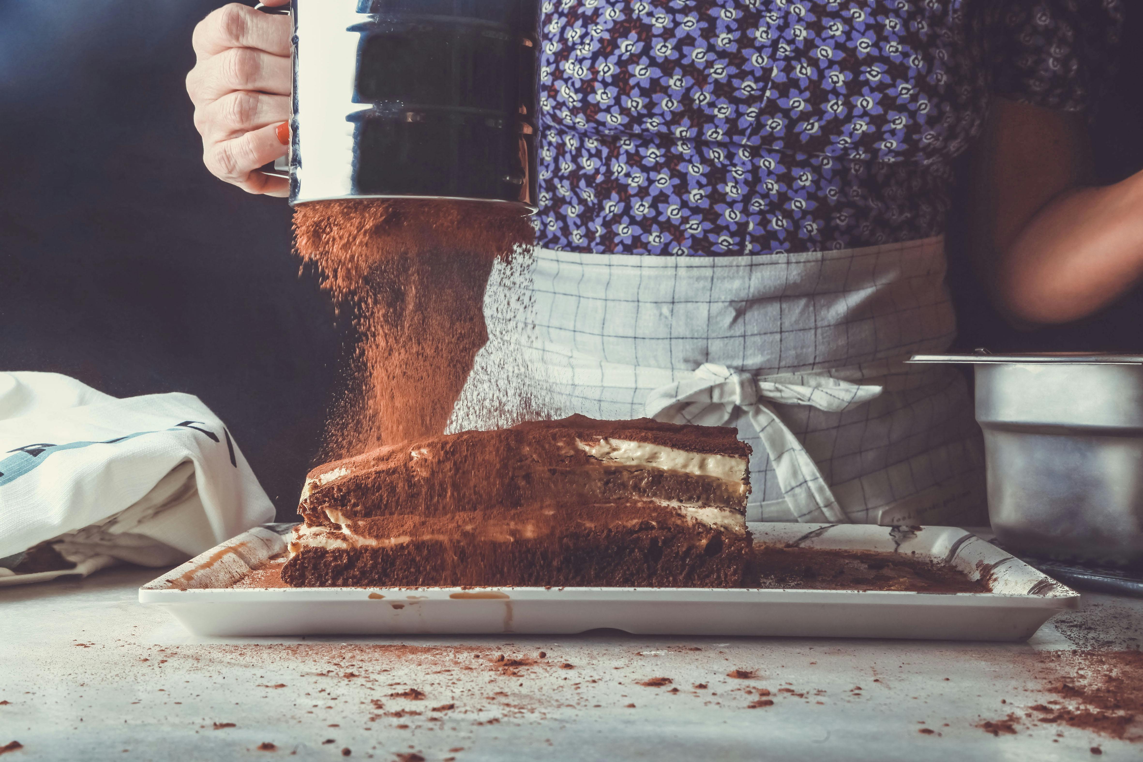 a person sifting cocoa powder over a cake