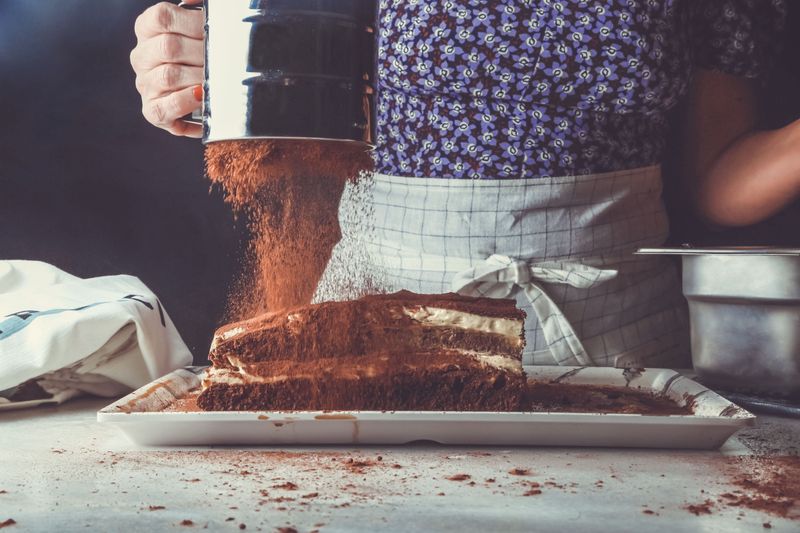 Artisan Luke Artisan Bakery menabur cocoa di atas cake