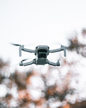 Low angle of professional unmanned drone flying over countryside against blurred trees at daytime
