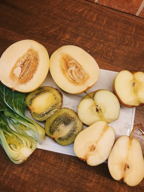 Free Top view halves of of apples and pears placed near kiwis and melons on table with green bok choy in kitchen Stock Photo