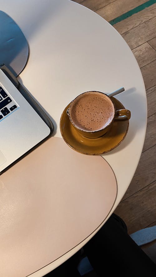 Free From above cup of freshly brewed coffee on plate placed on white table near modern netbook in light modern cafe Stock Photo