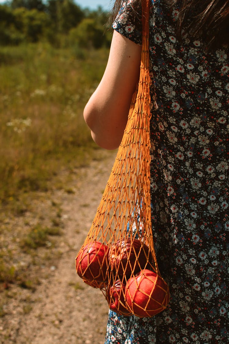 Unrecognizable Woman With String Bag Of Apples